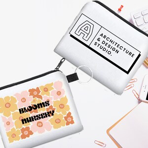 May include: Two white zippered pouches. One pouch has a floral pattern with the text "BLOOMS NURSERY". The other pouch has the text "ARCHITECTURE & DESIGN STUDIO."
