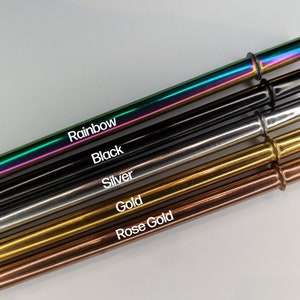 Op de afbeelding: Vijf drinkrietjes van roestvrij staal in verschillende kleuren: regenboog, zwart, zilver, goud en ros&eacute; goud. De rietjes zijn in een rij gerangschikt, met het regenboog rietje bovenaan en het ros&eacute; gouden rietje onderaan.