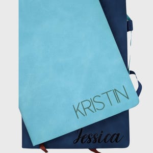 May include: Two blue notebooks with the names "Kristin" and "Jessica" written on them in different fonts and colors.