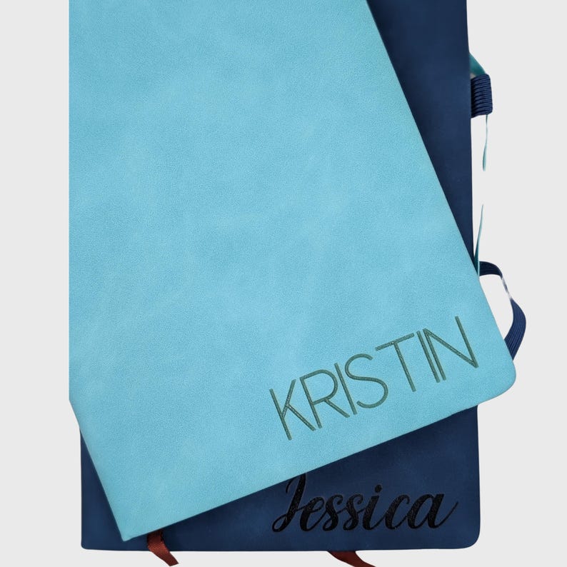 May include: Two blue notebooks with the names "Kristin" and "Jessica" written on them in different fonts and colors.