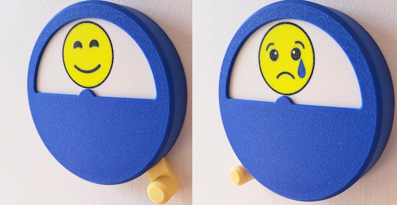 May include: Two blue round emotion dials with a yellow smiley face and a yellow sad face with a tear. The dials have a white background and a yellow knob.