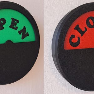 May include: A black and white sign with a rotating dial that says "OPEN" in green and "CLOSED" in red.