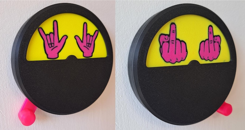 May include: Two black and yellow round wall-mounted signs with a pink hand gesture on each. The left sign has a pink hand making the rock and roll hand gesture. The right sign has a pink hand making the middle finger gesture. Both signs have a pink lever on the side.