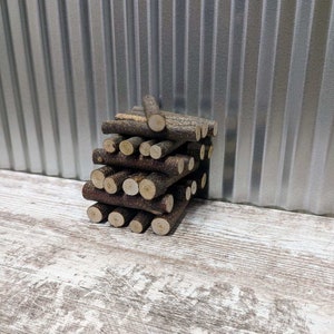May include: A stack of small, brown, wooden sticks arranged in a pyramid shape. The sticks are about 1 inch in diameter and 3 inches long. The sticks are on a white, wooden surface.
