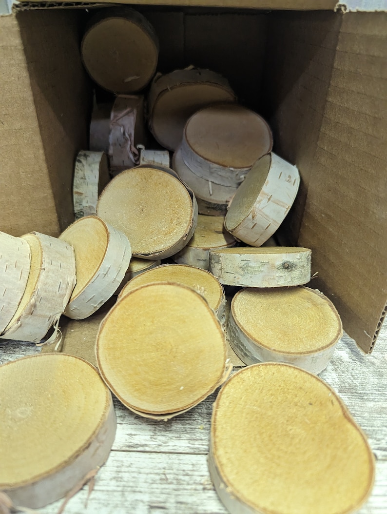 May include: A box filled with natural birch wood slices. The slices are various sizes and shapes, with a light brown colour and a natural wood grain pattern.