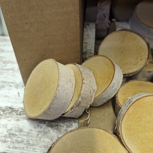 May include: A pile of natural wood slices, probably birch, with a light brown colour and a smooth, polished surface. The wood slices are stacked on top of each other and are arranged in a circular pattern. The wood slices are ideal for crafting projects, such as coasters, ornaments, or jewellery.