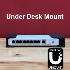 May include: A white network device with multiple ports, mounted in a black under-desk bracket. The text "Under Desk Mount" is above the device. A black and white logo with the text "Built For Ubiquiti" is on the right.