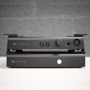 May include: Two black audio devices stacked on top of each other. The top device is labeled "MAGNIUS" and has a knob and buttons. The bottom device is labeled "MODIUS" and has a white light.