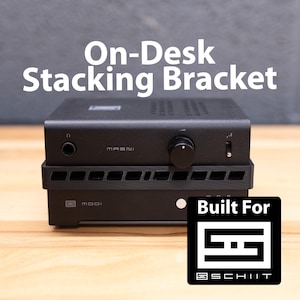 May include: Black on-desk stacking bracket for Schiit Audio components. The bracket is designed to stack two Schiit Audio devices, such as the Modi and Magni, on top of each other. The bracket is made of metal and has a black finish. Built For Schiit.