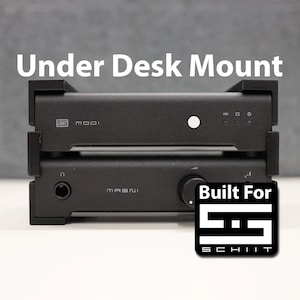 Może przedstawiać: Dwa czarne urządzenia audio, Schiit Modi i Schiit Magni, są ułożone jeden na drugim. Urządzenia są zamontowane na czarnym metalowym wsporniku. Tekst "Built For Schiit" jest nadrukowany na białej naklejce pod urządzeniami.
