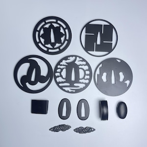 May include: A set of ten black metal sword fittings, including a variety of shapes and designs. The fittings are all made of a smooth, polished metal and have a traditional Japanese aesthetic.