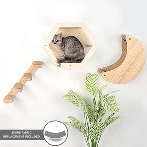 Puede incluir: Un condominio para gatos de madera con una ventana hexagonal, una cama con forma de luna creciente y una escalera con peldaños cubiertos de cuerda. El condominio está hecho de madera natural e incluye un repuesto de tela de repuesto. Un gato está sentado en la ventana del condominio.