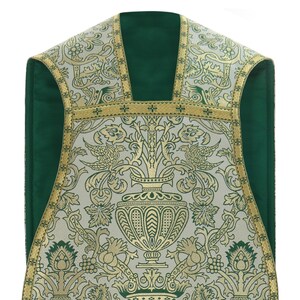 May include: A white and gold brocade chasuble with a green lining. The fabric features a floral pattern with birds and a central vase.