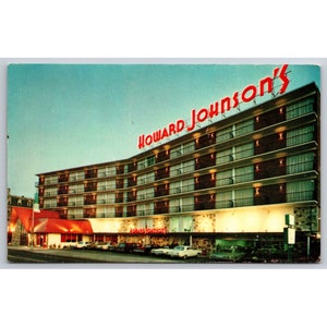 May include: A vintage postcard featuring a multi-story motel with the sign "Howard Johnson's" in red neon letters. The motel is lit up at night and has a red roof. There are cars parked in front of the motel.