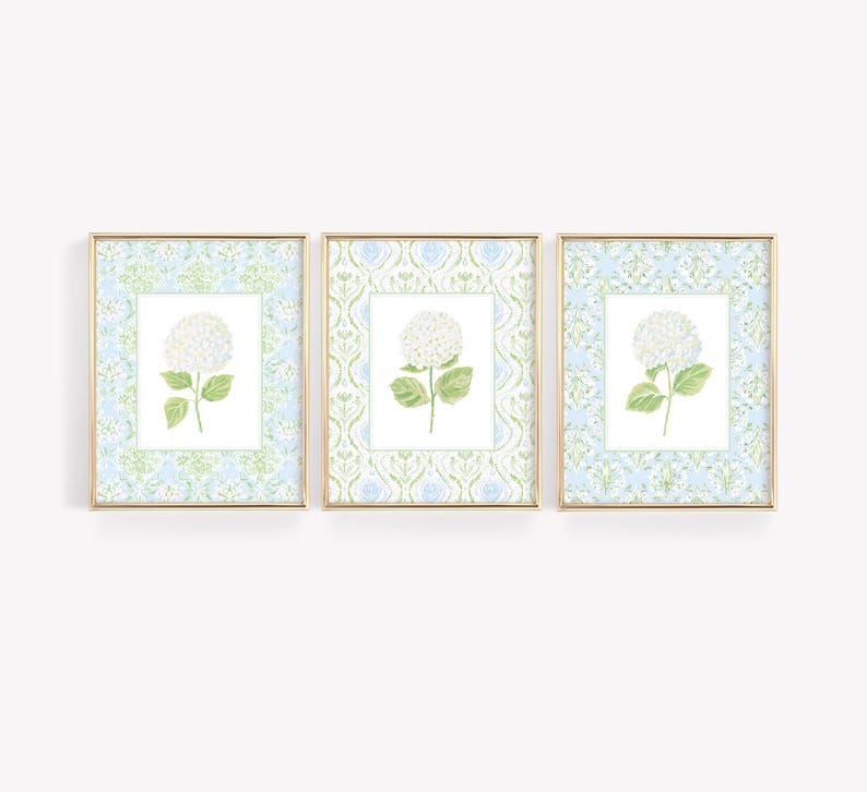 May include: A set of three framed wall art prints, each featuring a white hydrangea flower centred on a white background, surrounded by a light blue and green damask pattern border, all enclosed in thin gold-toned rectangular frames.