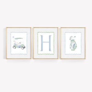 Puede incluir: Conjunto de tres láminas enmarcadas con temática de golf. Cada lámina presenta una ilustración en acuarela: un carrito de golf, la letra "H" y una bolsa de golf con palos. Las láminas tienen marcos dorados y un fondo blanco con lunares azules.