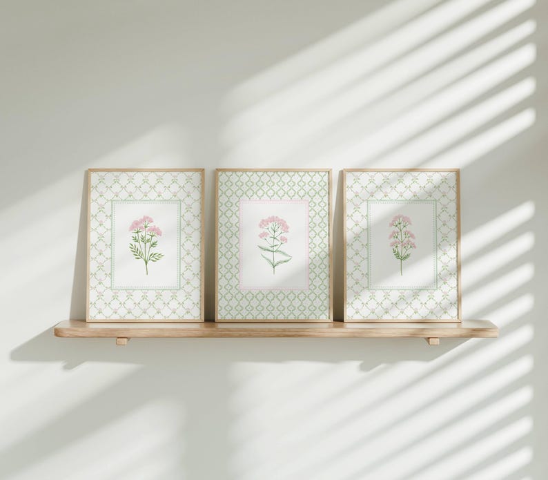 May include: Three framed prints with a white background and a green and white geometric pattern. Each print features a pink flower with green leaves.