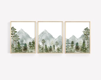 May include: A set of three watercolour prints depicting a mountain range with a forest in the foreground. The mountains are painted in shades of blue and green, and the trees are a deep green. The prints are framed in gold.