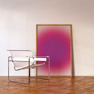 May include: A white leather and chrome lounge chair sits in front of a framed abstract painting with a pink and purple gradient. The painting is hanging on a white wall. The floor is made of wood planks.