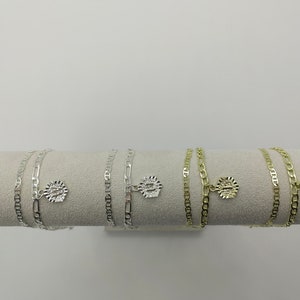 May include: Three silver and gold chain bracelets with a charm on each. The charms are round and have a textured design.