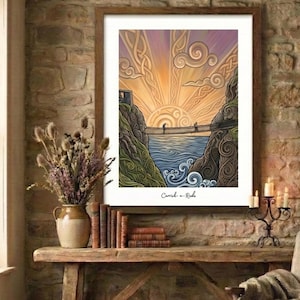 May include: Framed art print showing a suspension bridge over water with a sunset. The artwork features a bridge with two figures, cliffs, and stylized waves. The text "Carrick-a-Rede" is at the bottom of the print.