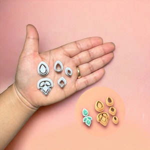May include: A set of six silver-colored cookie cutters shaped like different gemstones. The cutters are arranged in a hand, with the largest cutter in the center and the smallest cutter on the right. The cutters are made of metal and have a smooth, shiny finish.