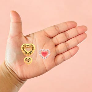 May include: Three gold heart-shaped charms with intricate designs. The largest charm has a barbed wire design, the middle charm has a geometric design, and the smallest charm has a simple heart design.