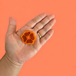 May include: Orange plastic flower cookie cutter in the shape of a poppy.