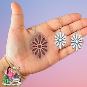 May include: A pink daisy-shaped cookie cutter and two daisy earrings with white petals and gold-colored posts are displayed. The earrings and cutter are held in a hand against a gradient pink and blue background.