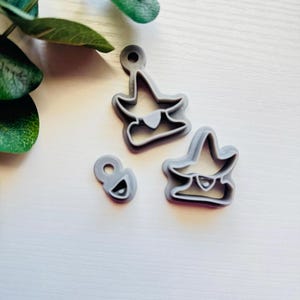 May include: Three gray plastic cookie cutters shaped like a wizard with a hat and beard. The cutters are on a white surface.