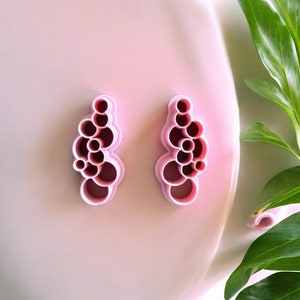 May include: A pair of pink plastic cookie cutters shaped like a cluster of bubbles.