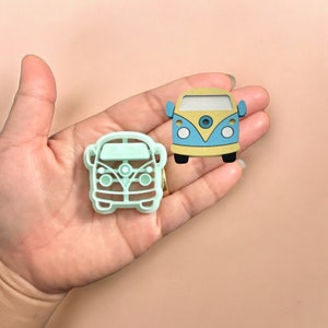 May include: A light blue and yellow cookie cutter shaped like a vintage Volkswagen van. The cookie cutter is made of plastic and has a detailed design.