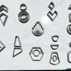 May include: A set of 15 silver-colored cookie cutters with various geometric shapes, including a hexagon, a crescent moon, a diamond, and a triangle.