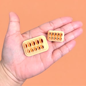 May include: Two peach-colored silicone tools with multiple holes, resembling a small brick, for creating designs in clay or fondant.