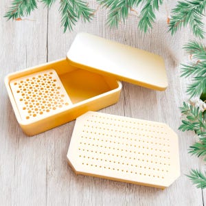 May include: A set of two yellow plastic containers with a grid pattern on the bottom. The containers are designed for storing small items.