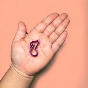 May include: A close-up of a pink plastic cookie cutter shaped like a treble clef.