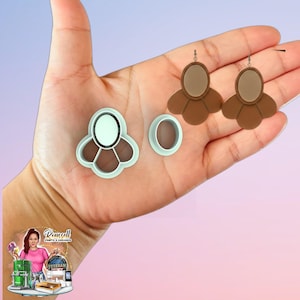 May include: A pair of brown and beige earrings with a matching flower-shaped cookie cutter and a small oval cutter. The earrings have a layered design with a beige oval center and brown petal-like shapes. The cutters are light blue.