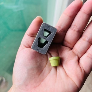 May include: A gray plastic mold with two empty pot shapes. A small, light green pot is next to the mold.