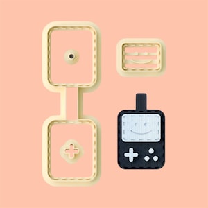 May include: A set of three cookie cutters in the shape of a retro video game console. The cutters are made of white plastic and have a stitched design. The console has a smiley face on the screen and a plus sign and three dots on the bottom.