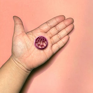 May include: A small, round, pink, 3D printed charm with a geometric design.