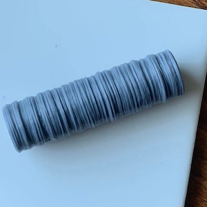 May include: A close-up of a gray, cylindrical object made of stacked, thin, flexible rings. The object is smooth and has a slightly textured surface.