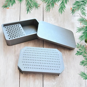 May include: A gray plastic box with a lid and a removable tray with a grid of small holes. The box is open and the tray is sitting on a wooden surface.