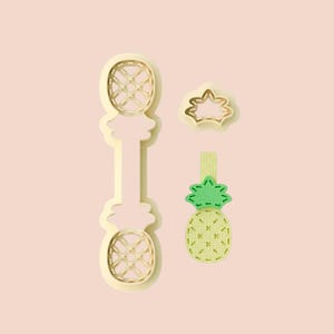 May include: A set of four pineapple-themed cookie cutters in various shapes. The cutters are in a light yellow color, with a green and yellow pineapple design. The shapes include a pineapple, a crown, and a pineapple on a stick.