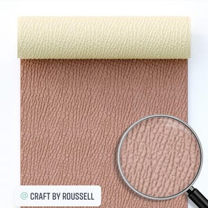 May include: A close-up of a roll of textured faux leather fabric in a light pink color. The fabric has a subtle embossed pattern that resembles the surface of leather. The fabric is rolled up and a magnifying glass is placed on top of the fabric to show the detail of the texture. The text "CRAFT BY ROUSSELL" is visible in the lower left corner of the image.