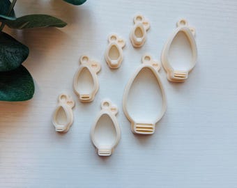 May include: Set of seven white plastic cookie cutters shaped like light bulbs, arranged on a white surface.
