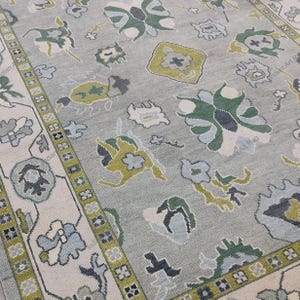 May include: A light gray rug with a floral pattern in shades of green, blue, and cream. The rug has a border with a repeating geometric design. The overall design is a traditional style.