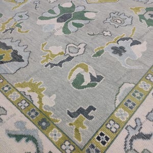 May include: A light blue rug with a floral pattern in shades of green, white, and yellow. The rug has a border with geometric designs. The rug is a decorative floor covering.