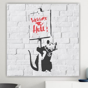 Può includere: Una stampa d'arte a stencil in bianco e nero di un ratto che tiene un cartello con su scritto "Benvenuti all'inferno!" Il ratto indossa una collana con un simbolo di pace e si trova di fronte a un muro di mattoni bianchi.