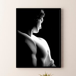 Könnte beinhalten: Schwarzweißfoto einer Marmorskulptur eines menschlichen Torsos. Die Skulptur ist seitlich beleuchtet, was einen dramatischen Kontrast zwischen Licht und Schatten erzeugt.