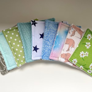 Puede incluir: Un conjunto de nueve cuadrados de tela con diferentes patrones, incluyendo estrellas, lunares y diseños florales. Los cuadrados son en tonos de verde, azul y rosa.